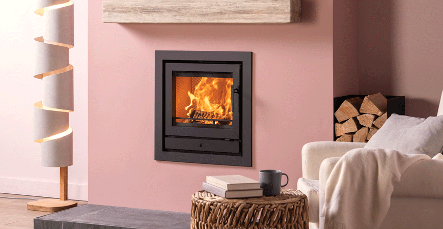 Log burner shown in a pink room with Barbiecore interior design trend. An inset wood burning stove.