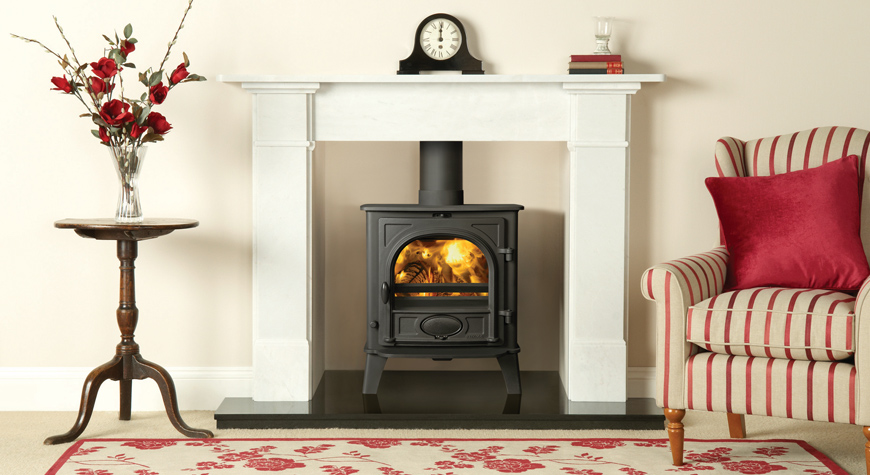 Multi-fuel version of the Stovax Stockton 5 stove with external riddling. Shown here in Matt Black, burning logs with Claremont Limestone mantel in White also available from Stovax.